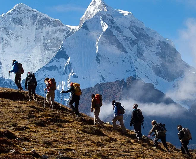 Trekker walking through a mountain trail surrounded by snow-capped peaks under a clear blue sky.